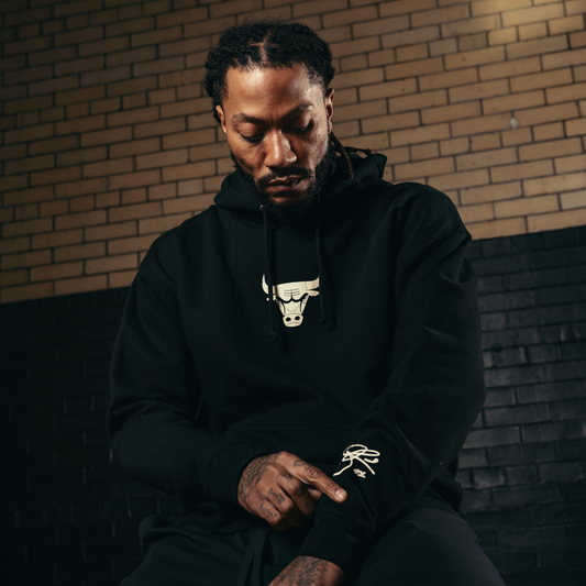 Rose wearing a black hoodie with a logo, sitting against a brick wall.