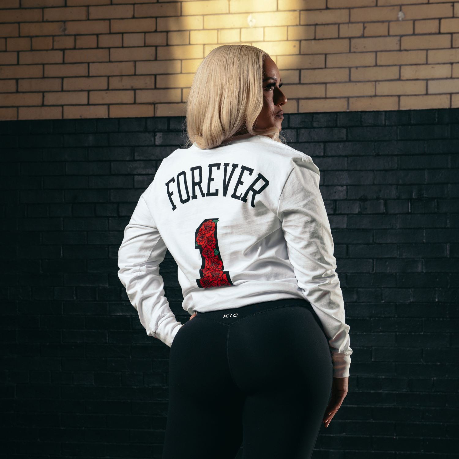 Person wearing a white jacket with 'FOREVER 1' text, standing against a brick wall.