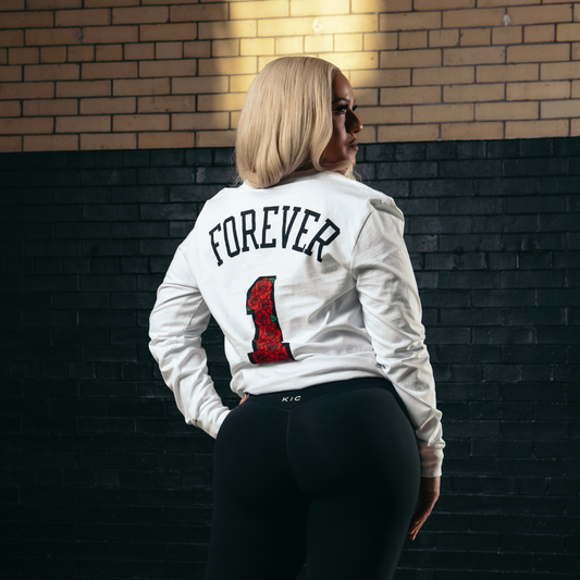 Person wearing a white jacket with 'FOREVER 1' text, standing against a brick wall.