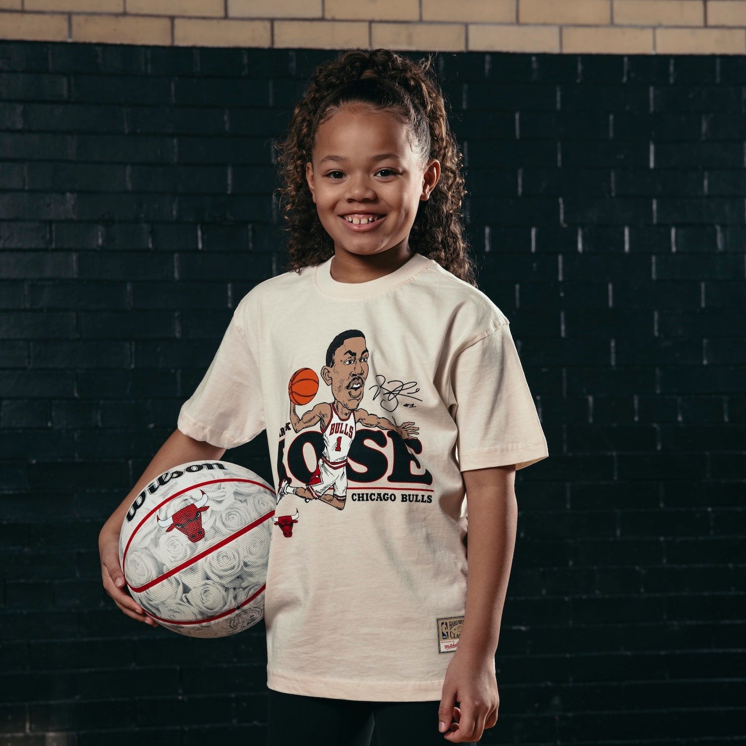 Child holding a basketball with a graphic t-shirt against a brick wall.