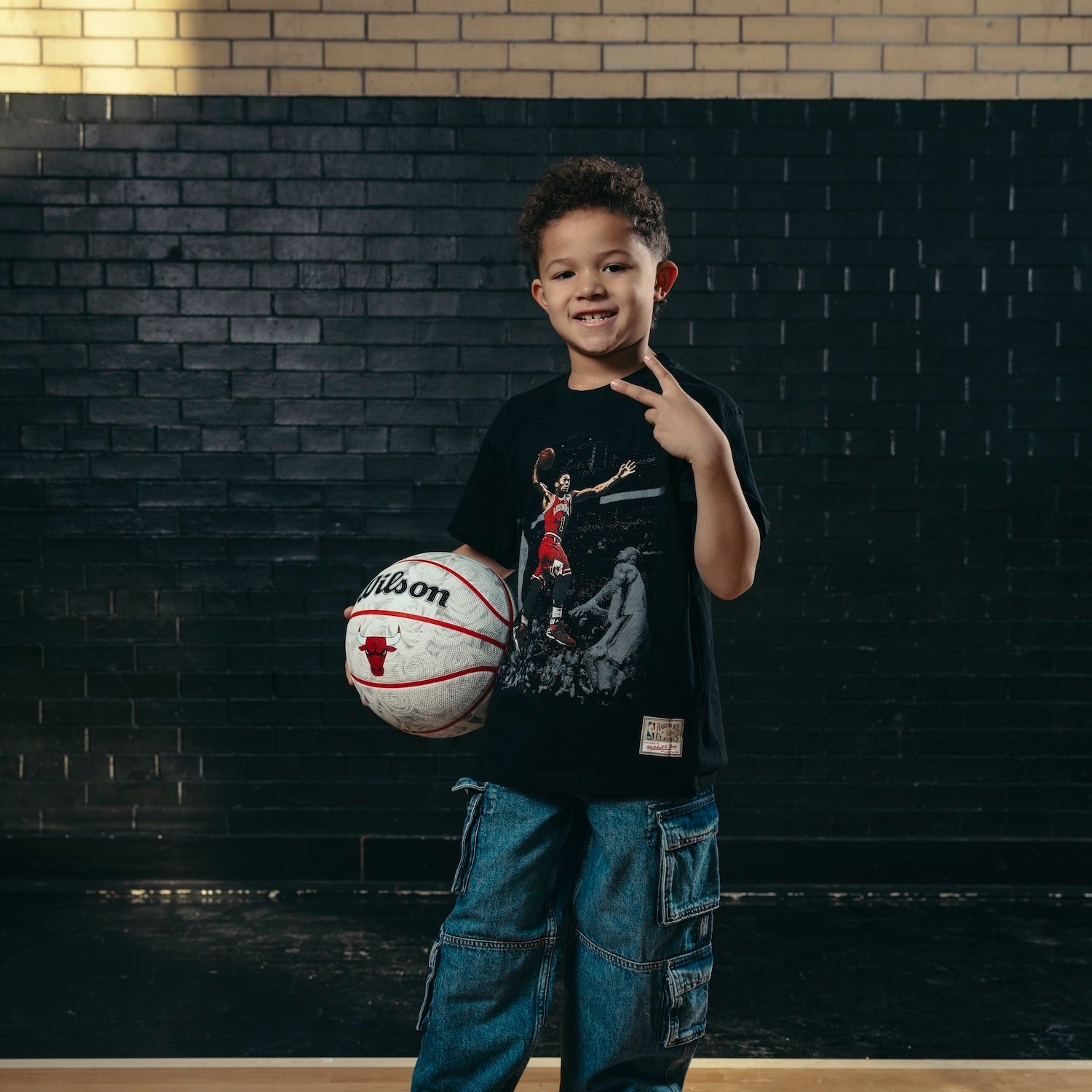 Child holding a basketball against a brick wall background